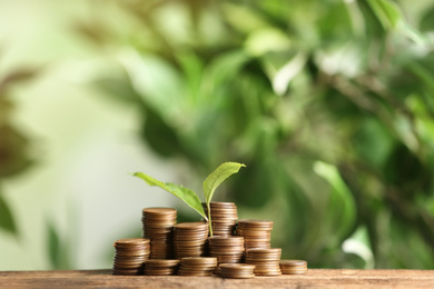 Coins and green sprout on wooden table against blurred background. Money savings
