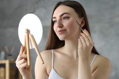 Photo of Beautiful woman drawing freckles with pen in front of little mirror indoors