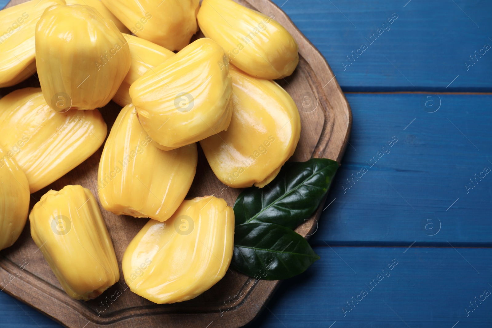 Photo of Delicious exotic jackfruit bulbs on blue wooden table, top view