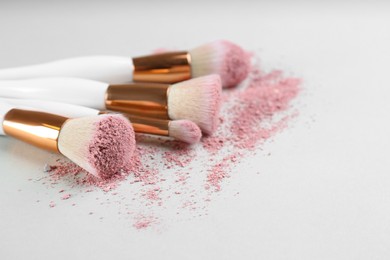 Photo of Different makeup brushes with crushed cosmetic product on light background, closeup. Space for text