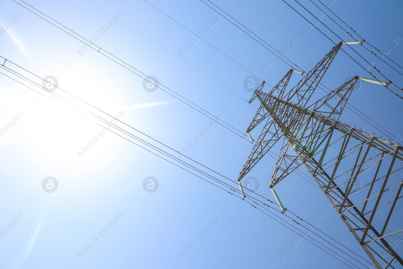 Photo of High voltage tower with electricity transmission power lines against blue sky, low angle view