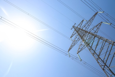 High voltage tower with electricity transmission power lines against blue sky, low angle view