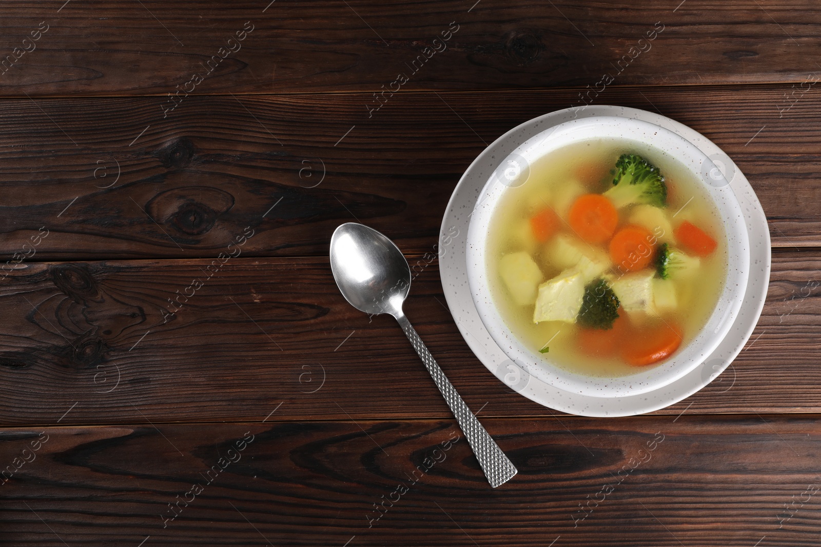 Photo of Tasty chicken soup with vegetables in bowl served on wooden table, top view. Space for text