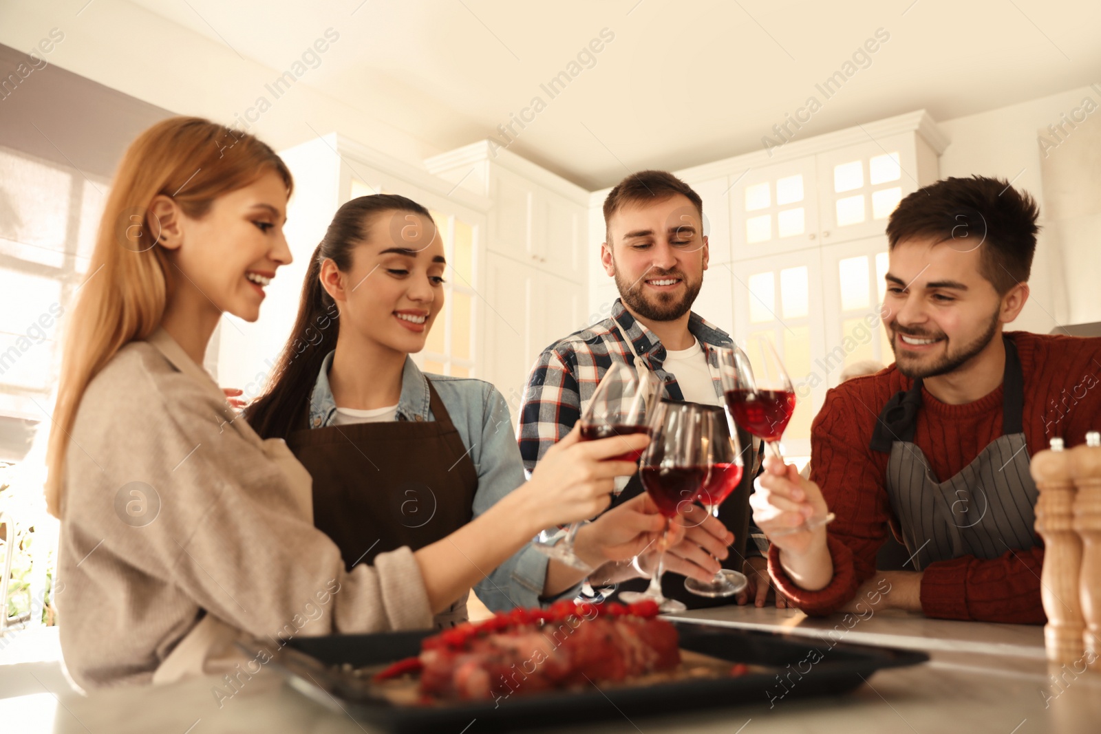 Photo of Happy people drinking wine while cooking food in kitchen