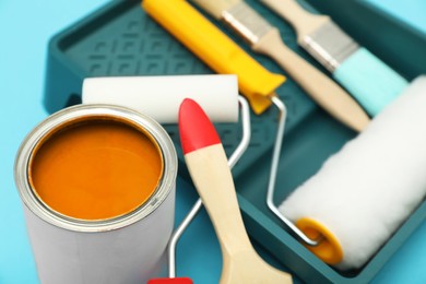 Can of orange paint, brushes, rollers and container on turquoise background, closeup