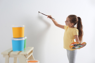 Photo of Little child painting on blank white wall indoors
