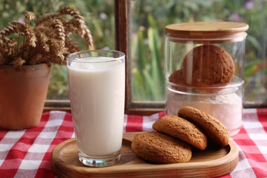 Photo of Glass of milk with cookies on red checkered tablecloth indoors
