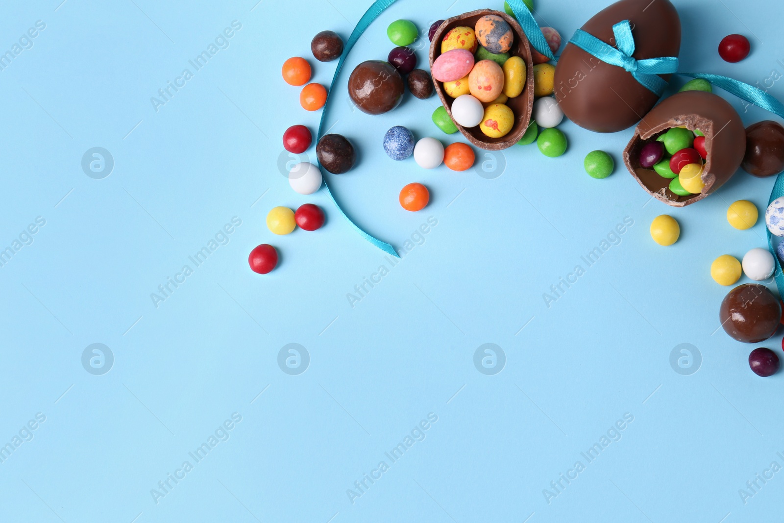 Photo of Flat lay composition with tasty chocolate eggs and different candies on light blue background. Space for text