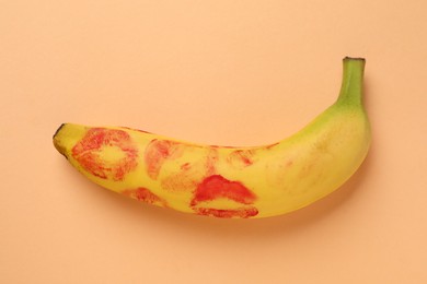 Photo of Banana with red lipstick marks on pale orange background, top view. Sex concept