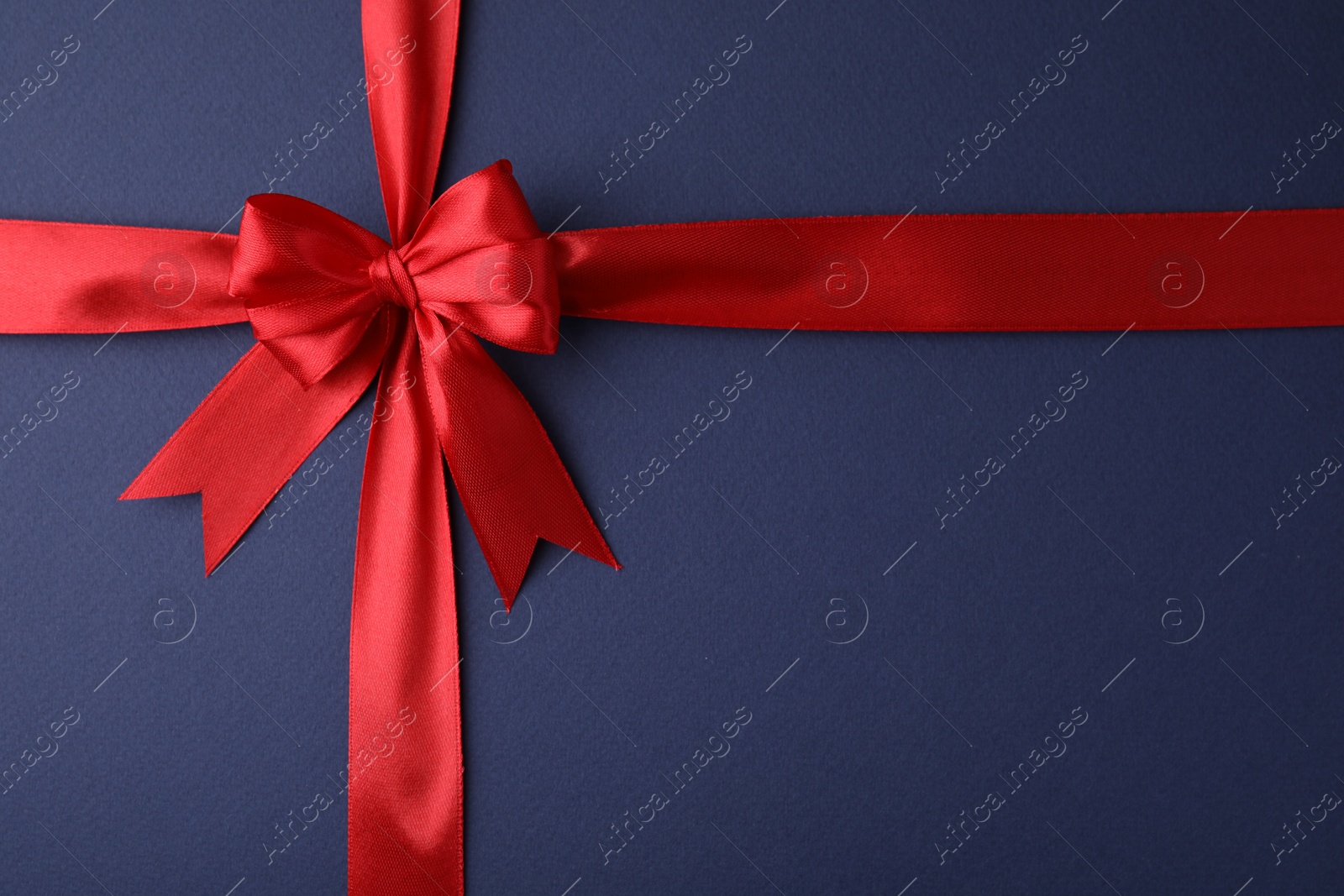 Photo of Red satin ribbon with bow on blue background, top view