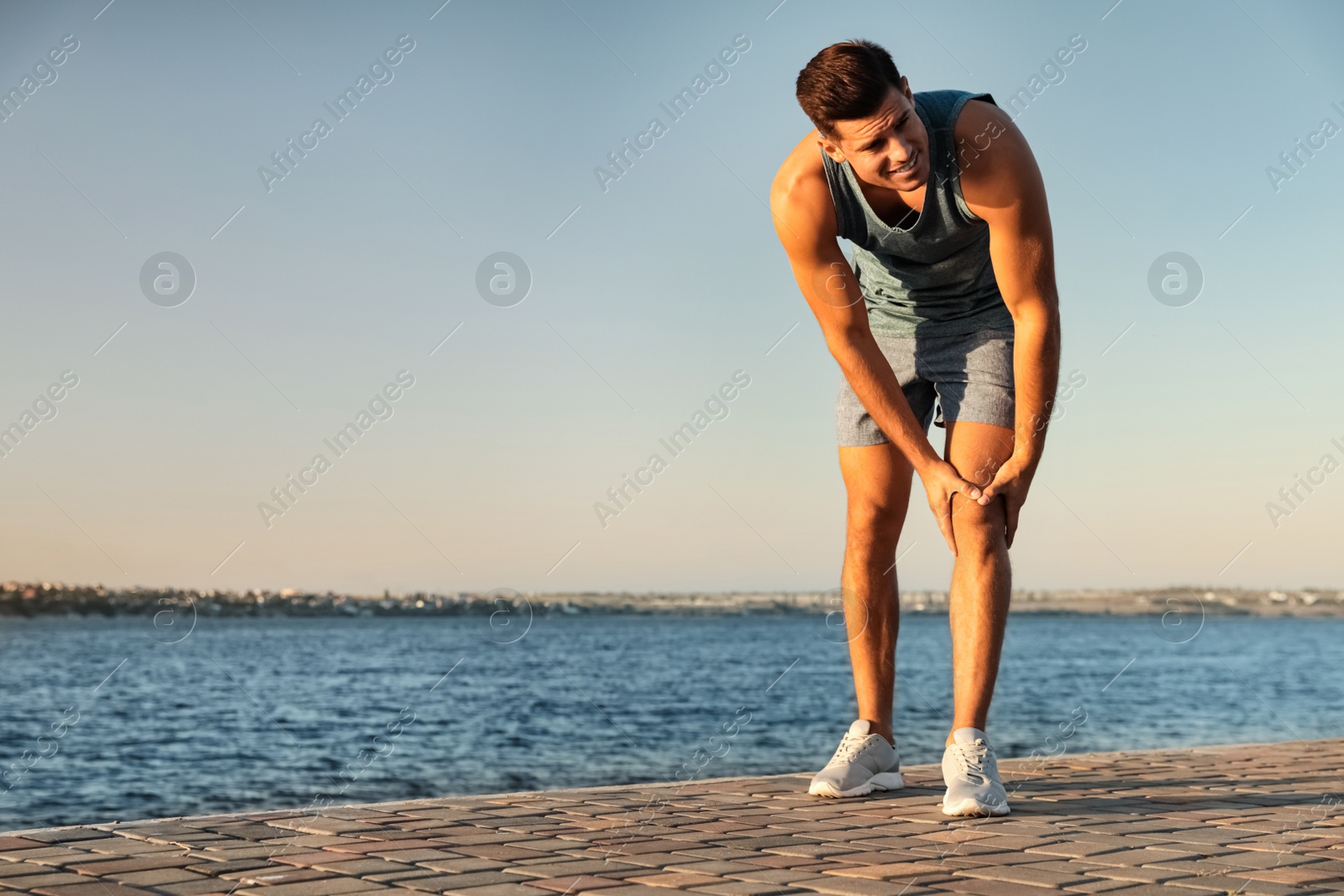 Photo of Man in sportswear having knee problems near river at sunset