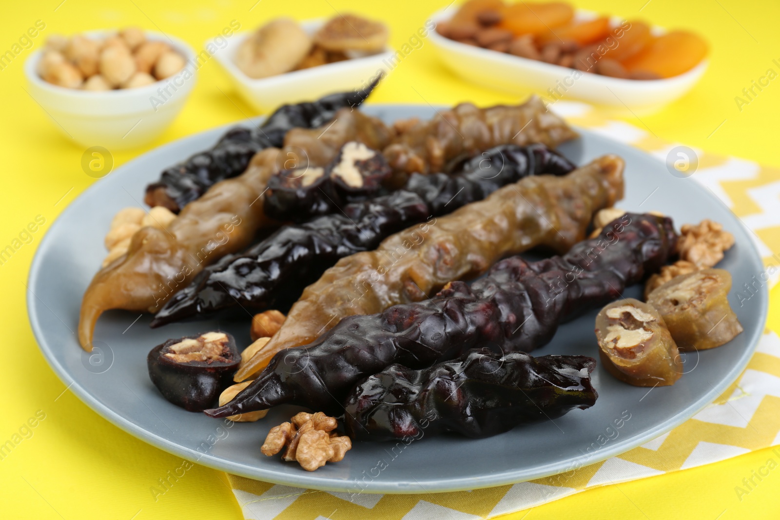 Photo of Plate with delicious churchkhelas, nuts and dried fruits on yellow background, closeup