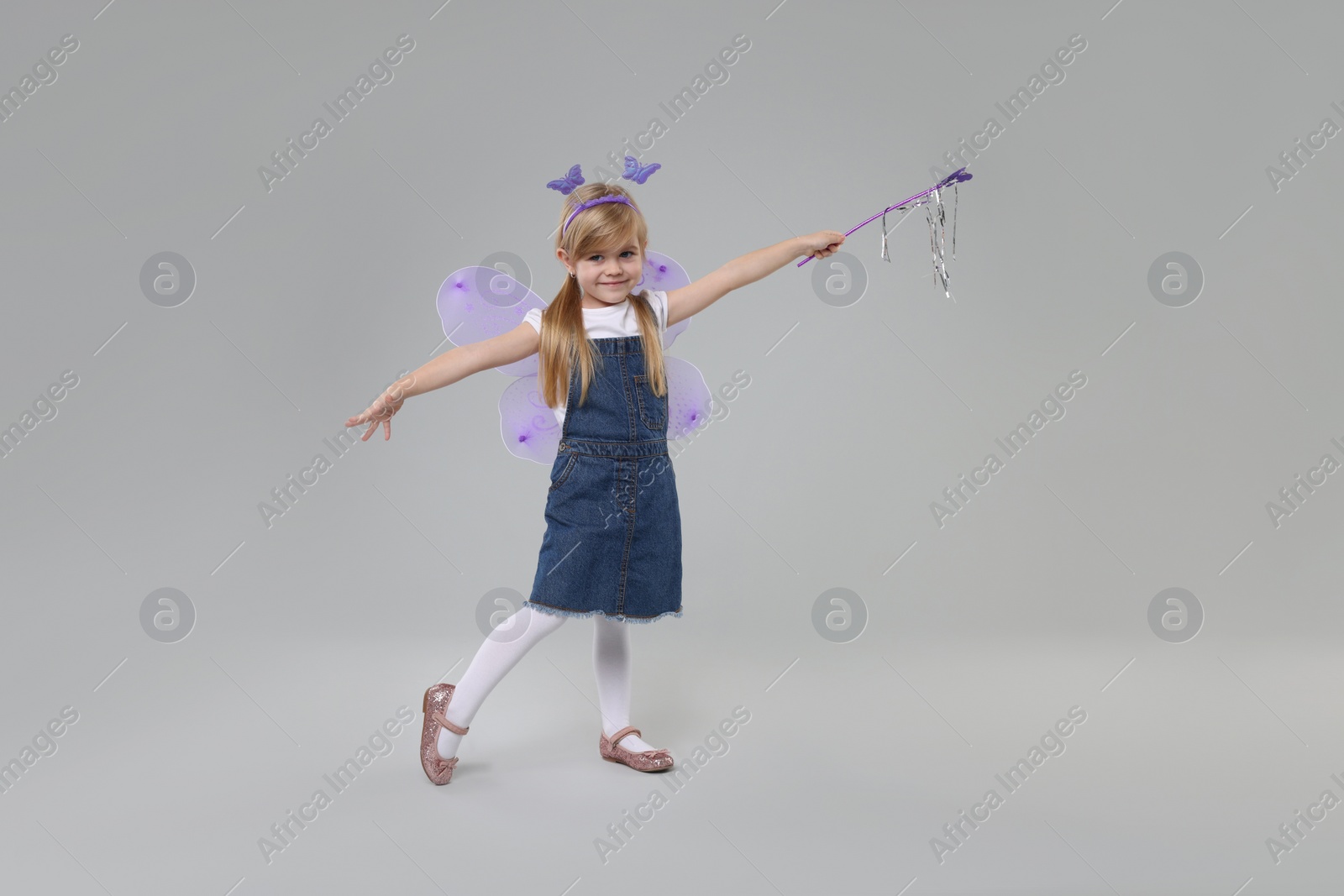 Photo of Cute little girl in fairy costume with violet wings and magic wand on light grey background