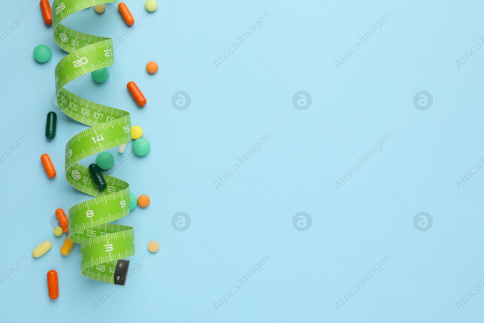 Photo of Different weight loss pills and measuring tape on light blue background, flat lay. Space for text