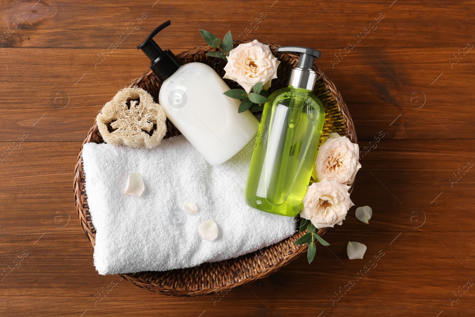 Photo of Dispensers of liquid soap, towel and roses in wicker basket on wooden table
