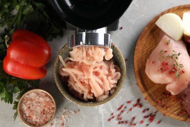 Electric meat grinder with chicken mince and products on grey marble table, flat lay