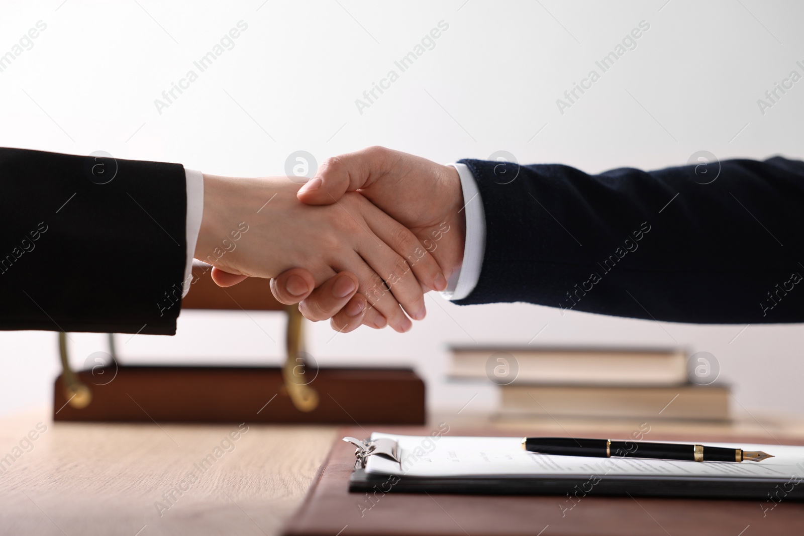 Photo of Notary shaking hands with client at wooden table in office, closeup