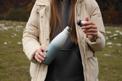 Photo of Woman holding thermo bottle with drink and cap in beautiful mountains, closeup