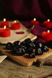 Photo of Many black rune stones and burning candles on wooden table