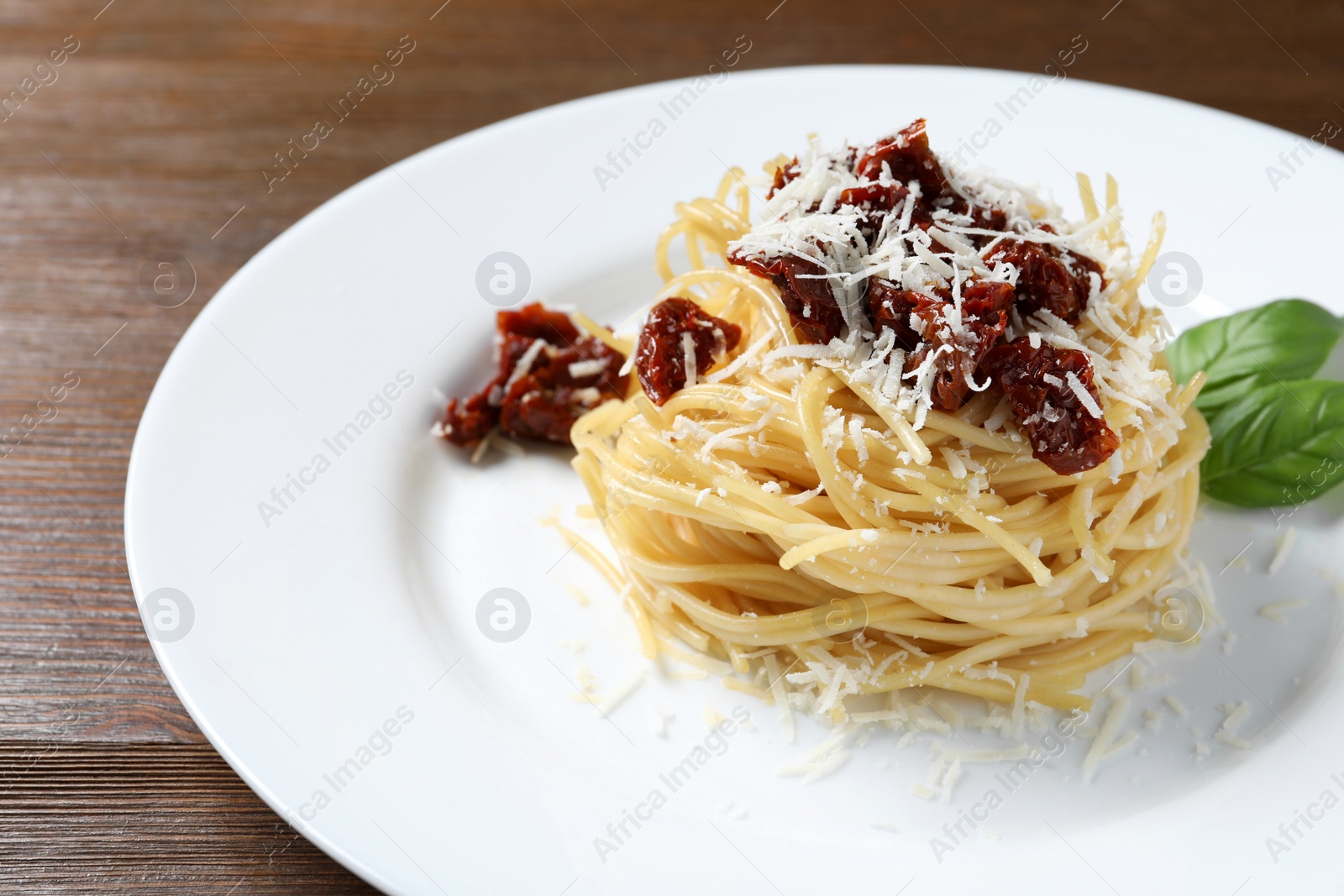 Photo of Tasty spaghetti with sun-dried tomatoes and parmesan cheese on wooden table, closeup. Exquisite presentation of pasta dish