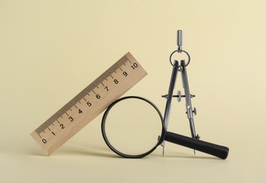 Ruler, magnifying glass and compass on yellow background
