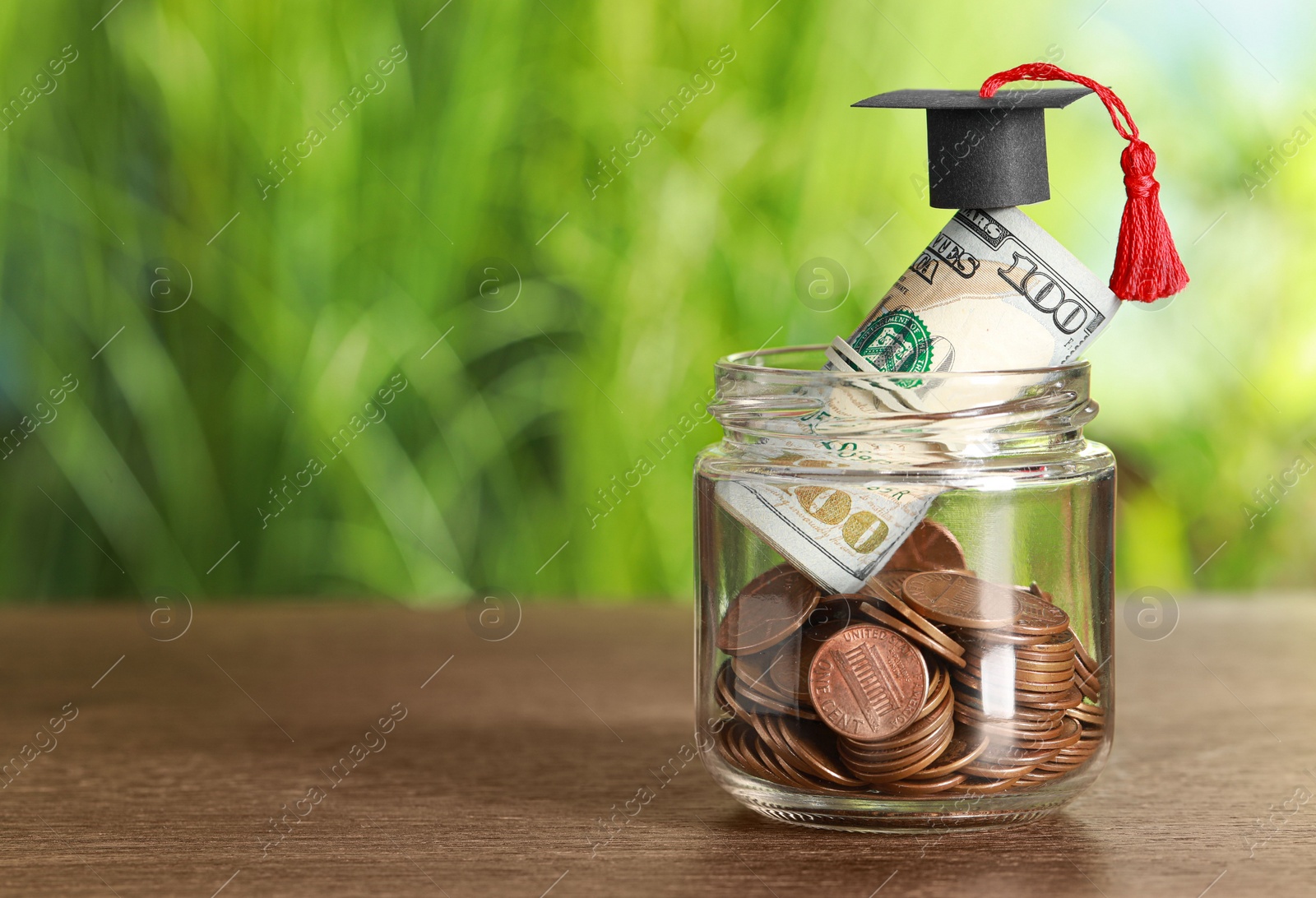 Photo of Scholarship concept. Glass jar with coins, dollar banknotes and graduation cap on wooden table, space for text