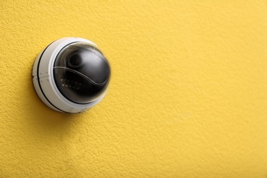 Photo of Modern CCTV security camera on yellow wall. Space for text