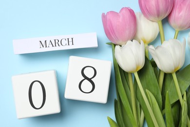 Photo of International Women's day - 8th of March. Wooden block calendar and beautiful flowers on light blue background, flat lay