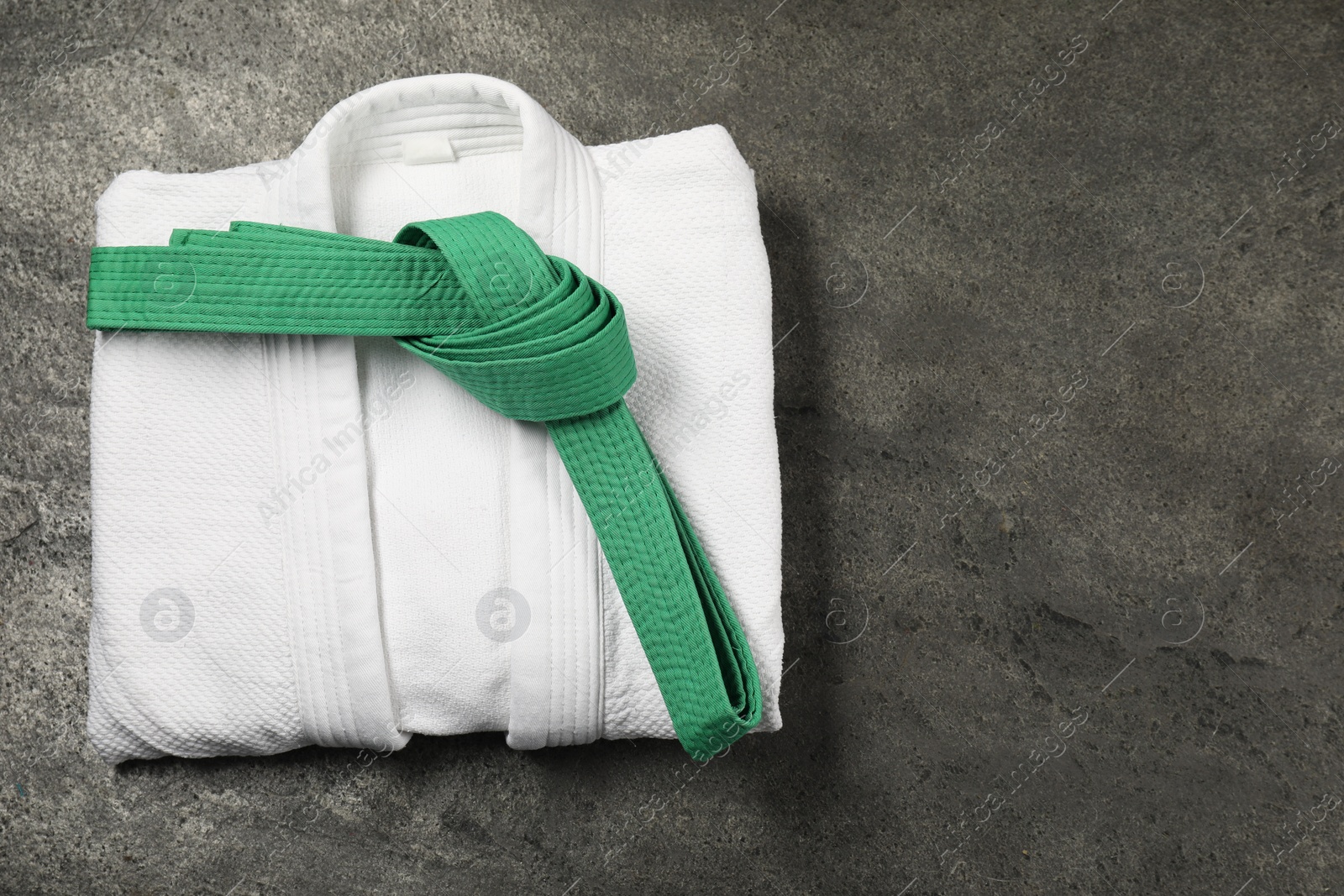 Photo of Green karate belt and white kimono on gray textured background, top view. Space for text