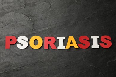 Word Psoriasis made of paper letters on dark gray textured table, top view