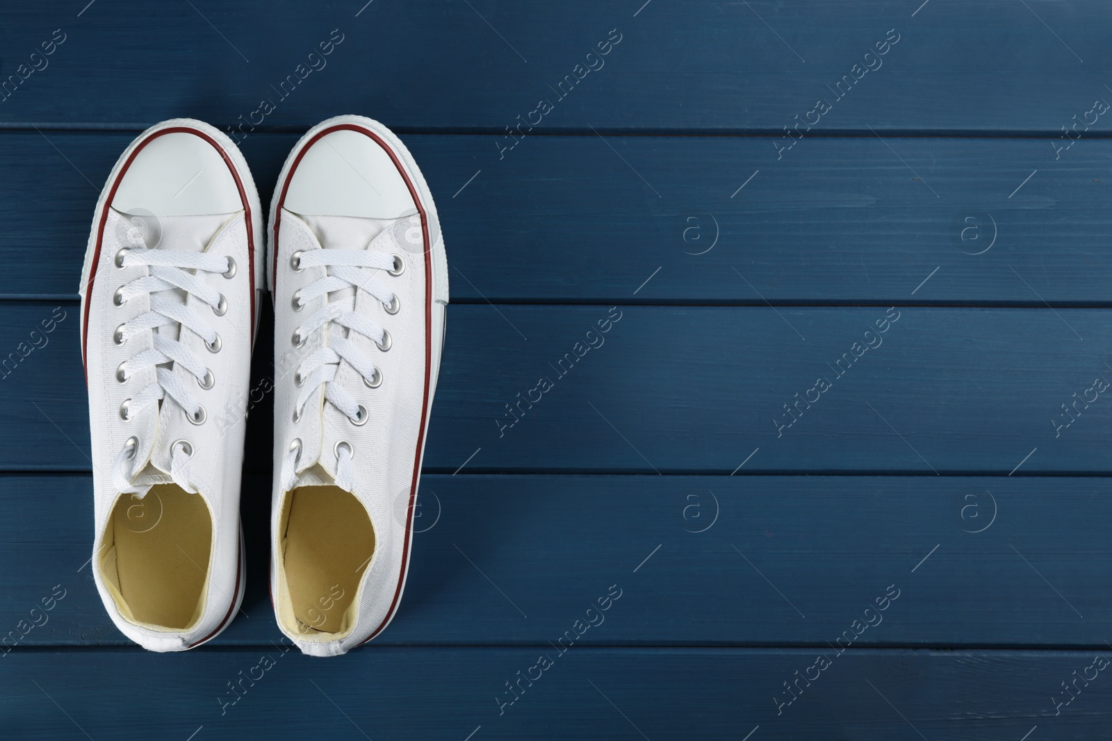 Photo of Pair of white sneakers on blue wooden table, flat lay. Space for text