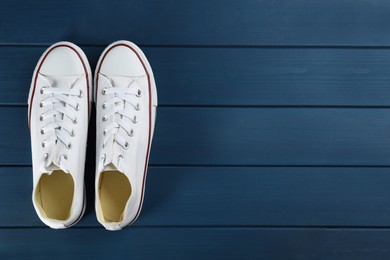Photo of Pair of white sneakers on blue wooden table, flat lay. Space for text