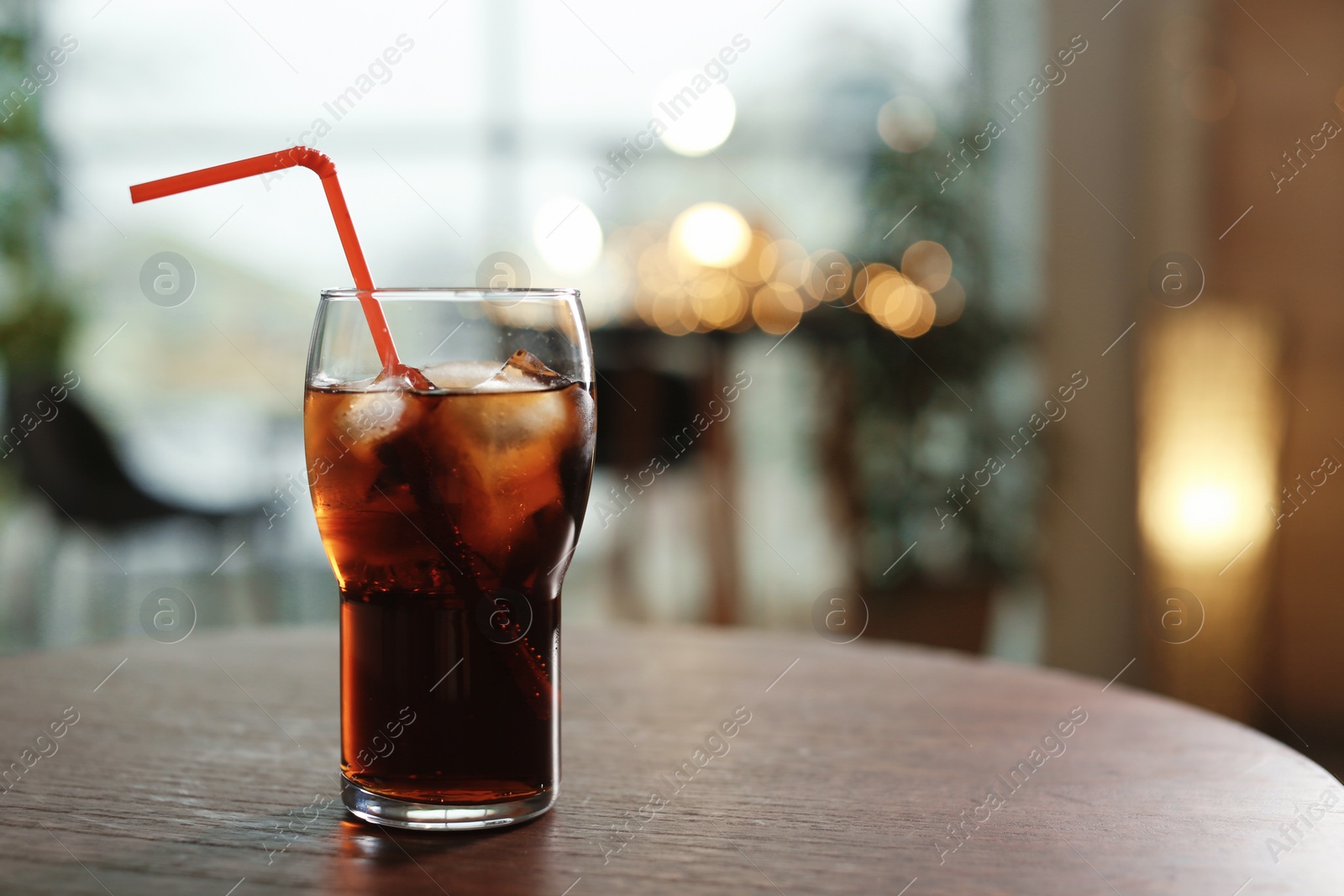 Photo of Glass of cold cola on table against blurred background. Space for text