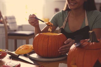 Photo of Woman making pumpkin jack o'lantern at table in kitchen, closeup. Halloween celebration