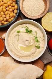 Delicious hummus with microgreens and different ingredients on wooden table, flat lay