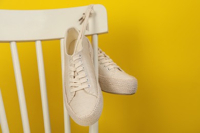 Photo of Pair of stylish sneakers hanging on white chair against yellow background. Space for text