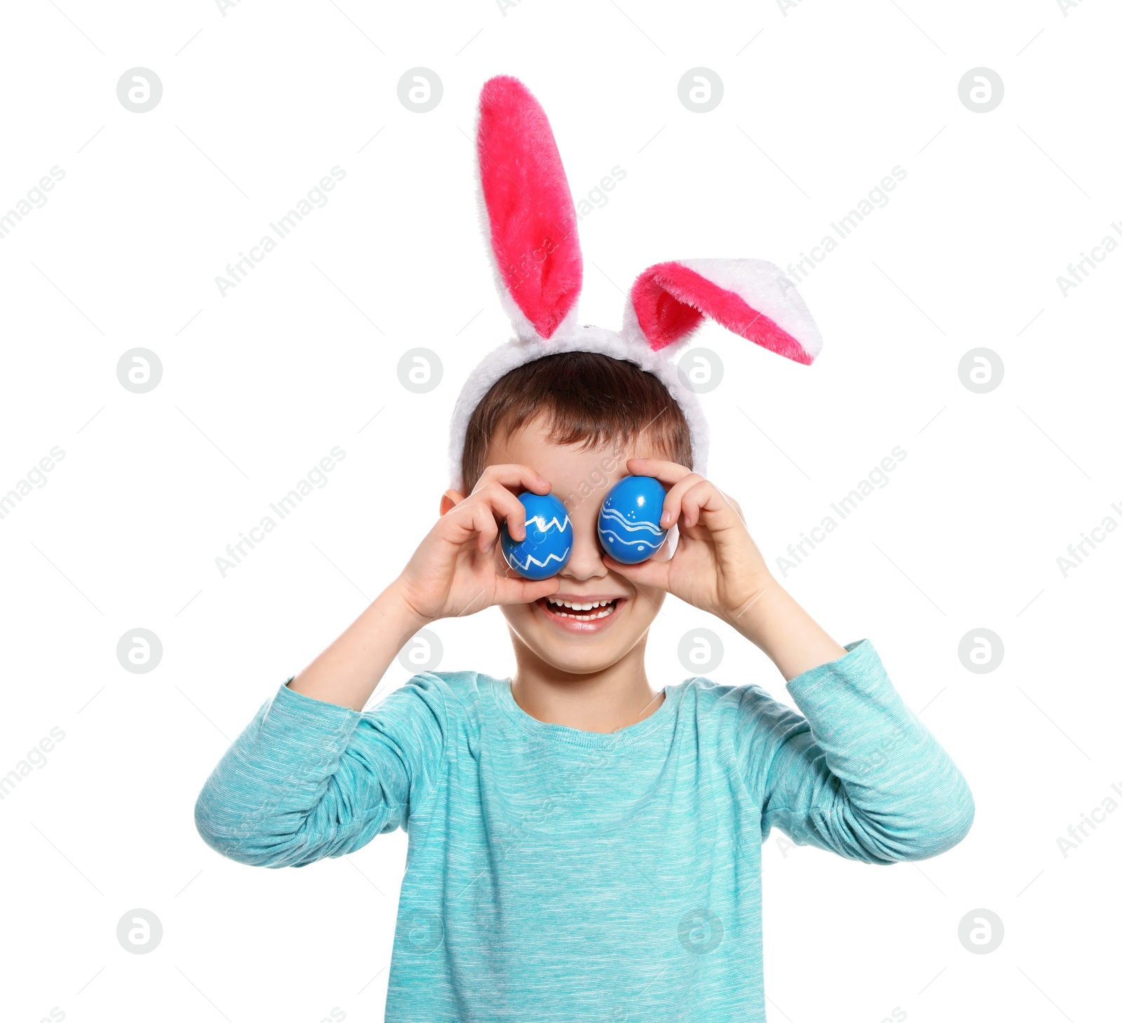 Photo of Little boy in bunny ears headband holding Easter eggs near eyes on white background