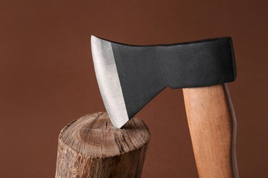 Photo of Metal axe in wooden log on brown background, closeup