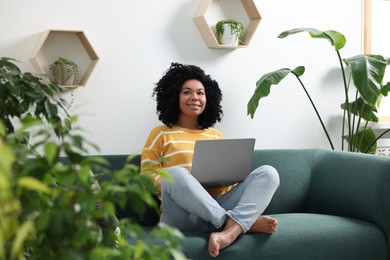 Relaxing atmosphere. Happy woman with laptop on sofa near beautiful houseplants in room