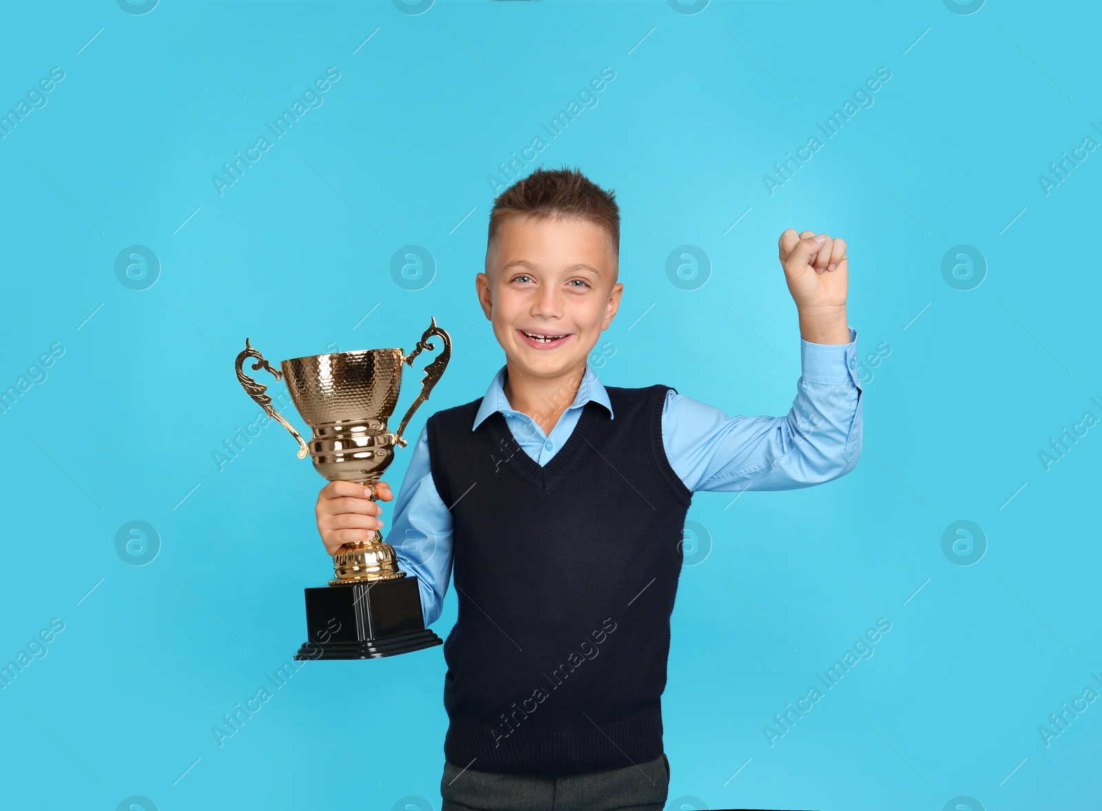 Photo of Happy boy in school uniform with golden winning cup on blue background. Space for text