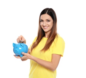 Young woman putting coin into piggy bank on white background