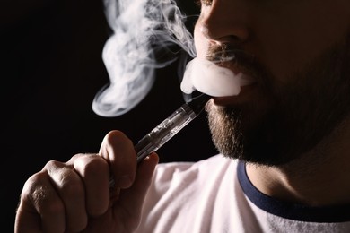 Photo of Man using electronic cigarette on black background, closeup