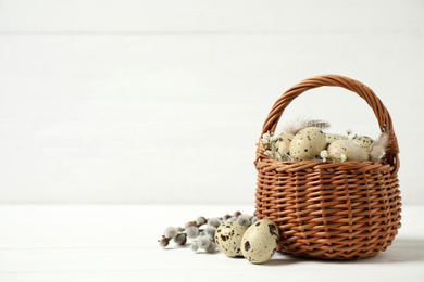 Photo of Quail eggs and flowers in wicker basket on white wooden table, space for text. Easter celebration