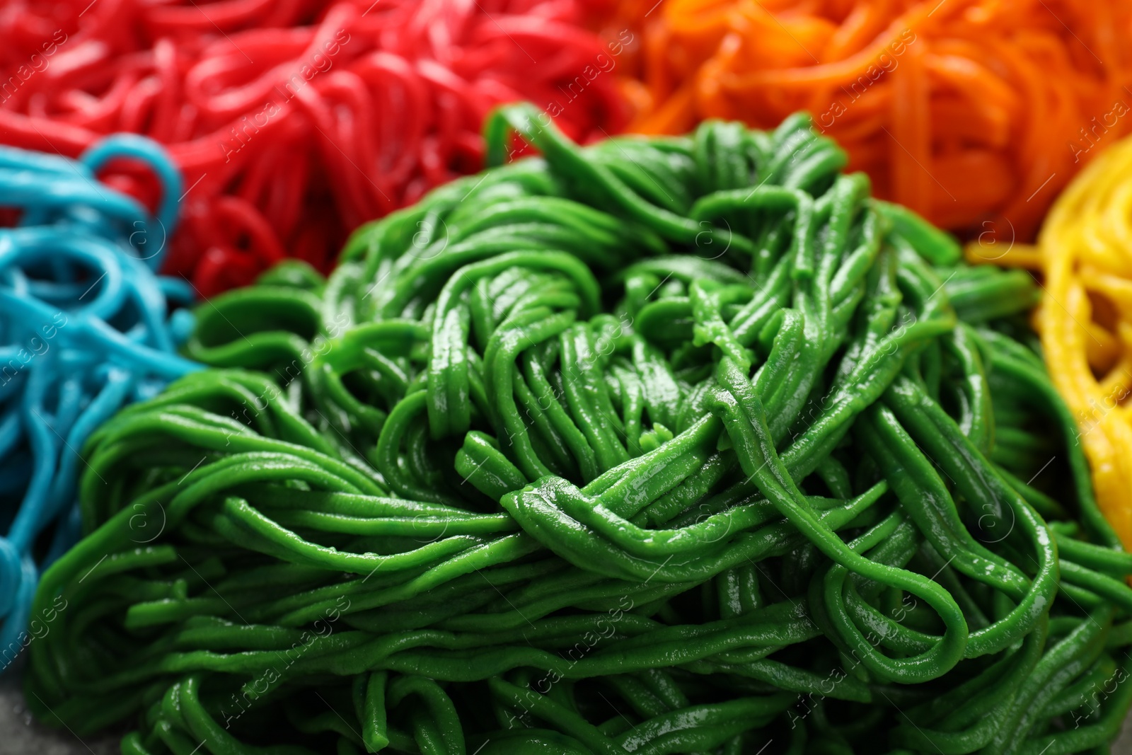 Photo of Rolled spaghetti painted with different food colorings as background, closeup