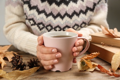 Woman with cup of hot drink at wooden table, closeup. Cozy autumn atmosphere