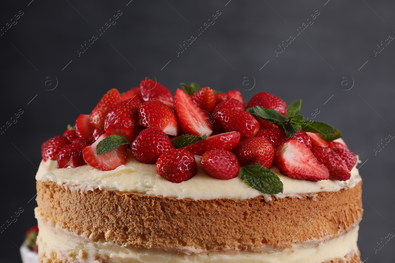 Photo of Tasty cake with fresh strawberries and mint on dark gray background, closeup