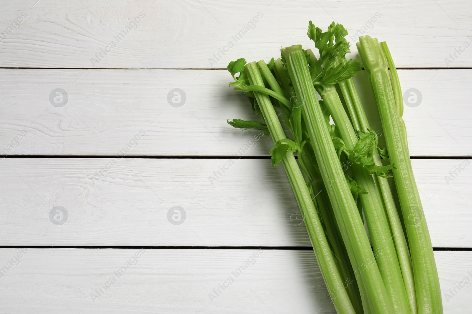 Photo of Fresh celery stalks on white wooden table, top view. Space for text