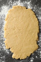 Photo of Shortcrust pastry. Raw dough and flour on grey table, top view