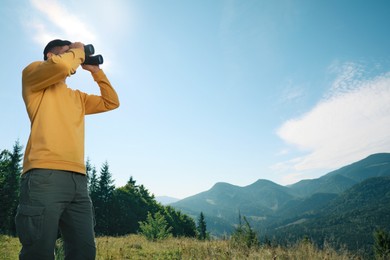 Photo of Man with binoculars in mountains on sunny day, low angle view. Space for text