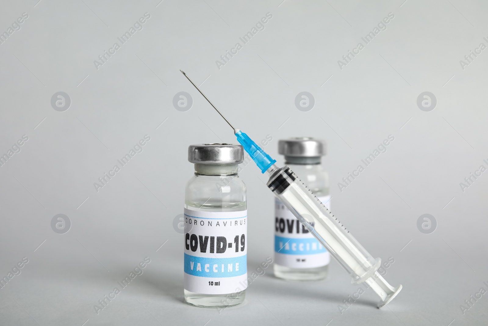 Photo of Vials with coronavirus vaccine and syringe on light background